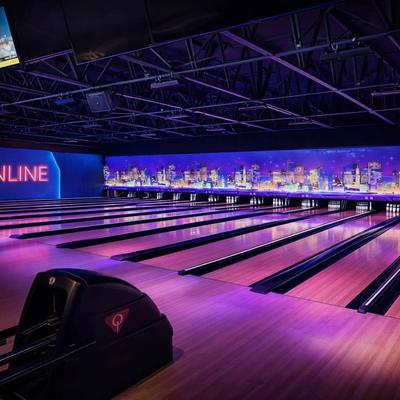 Modern bowling alley with purple cosmic lighting and a city skyline mural.