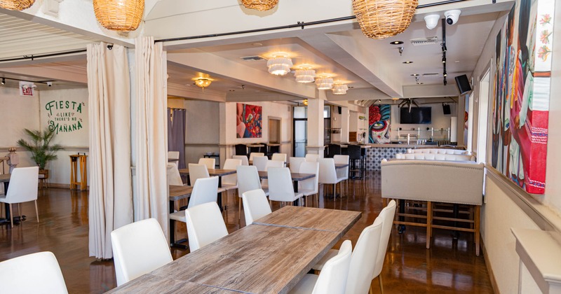 A modern restaurant interior with wooden tables, white leather chairs, basket lights