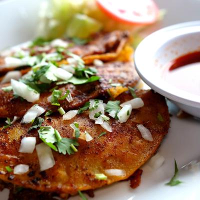 Taco Birria topped with onion and cilantro, served with a dip and fresh veggies.