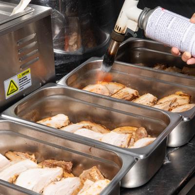 Slices of pork in metal trays being torched.