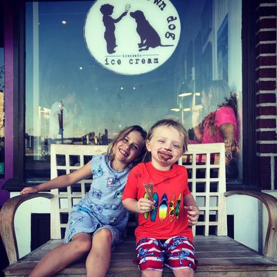 Two smiling children sit on a bench outside Brown Dog ice cream shop.
