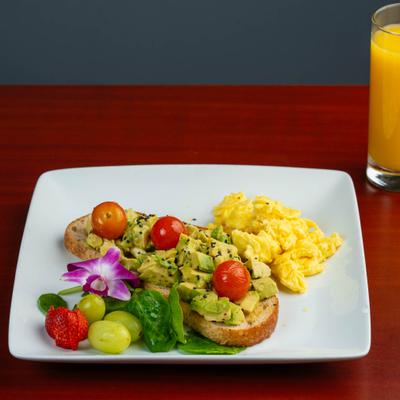 Avacado Toast topped with cherry tomatoes and served alongside scrambled eggs.