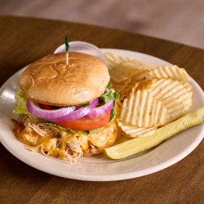 Shredded chicken taco sandwich served with chips and a pickle.