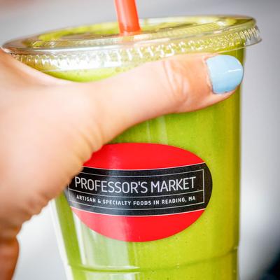 A cup of green smoothie in hand, close up.