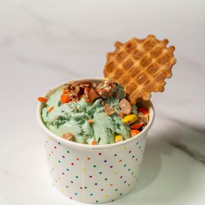 Mint chocolate chip ice cream in a paper cup topped with chocolate-covered candies.