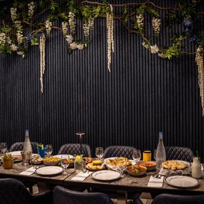A table with various Indian dishes in a modern setting featuring a dark wall and hanging flowers.