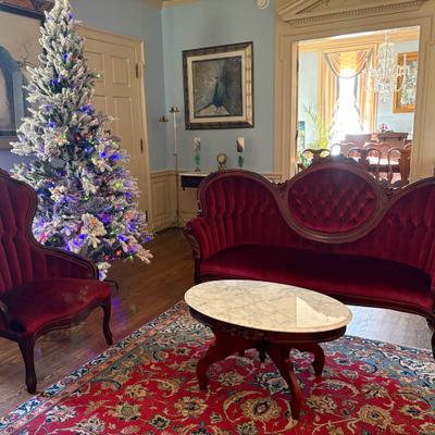 Living room interior with red velvet furniture, marble coffee table, and Christmas tree.