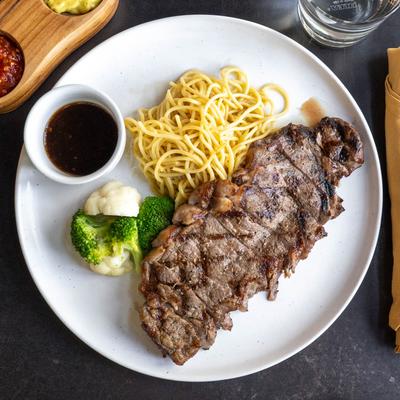 Steak with pasta, sauce, broccoli, and cauliflower on a white plate.