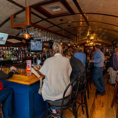 Crowded bar area,  glasses on a hanging wine glass rack, liquor bottles.
