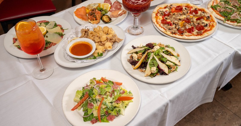 A table filled with various dishes and drinks, featuring appetizers, salads, and pizzas