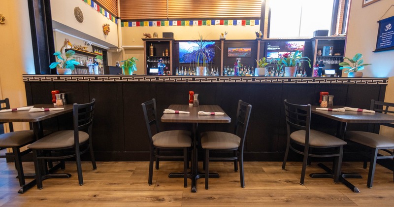 Interior of a restaurant with tables, chairs, wooden floor, and a counter with decorative items and plants
