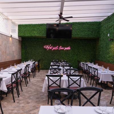 Patio's dining area with green faux-plant wall with neon sign that reads 
