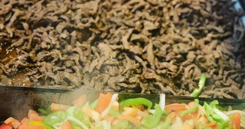 Cooked beef and mixed peppers sizzling on a hot grill