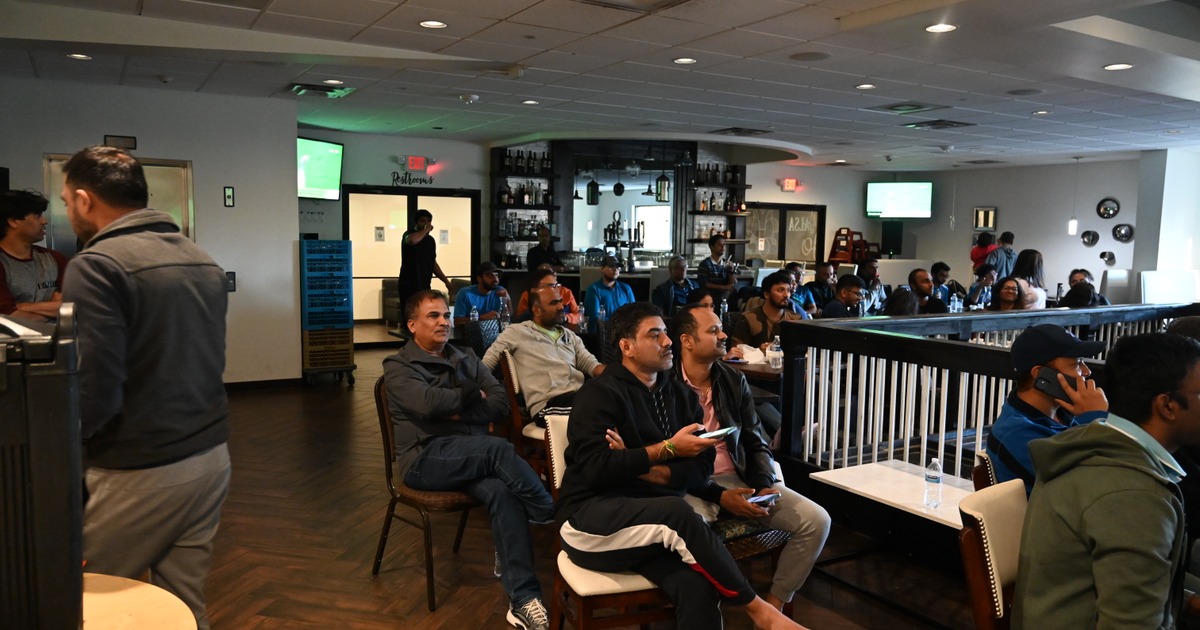 A group of people sit in a lounge or bar with a relaxed atmosphere, watching a game