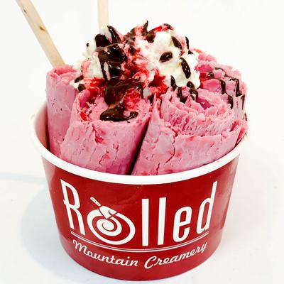 Pink ice cream topped with brownie pieces in a red cup.