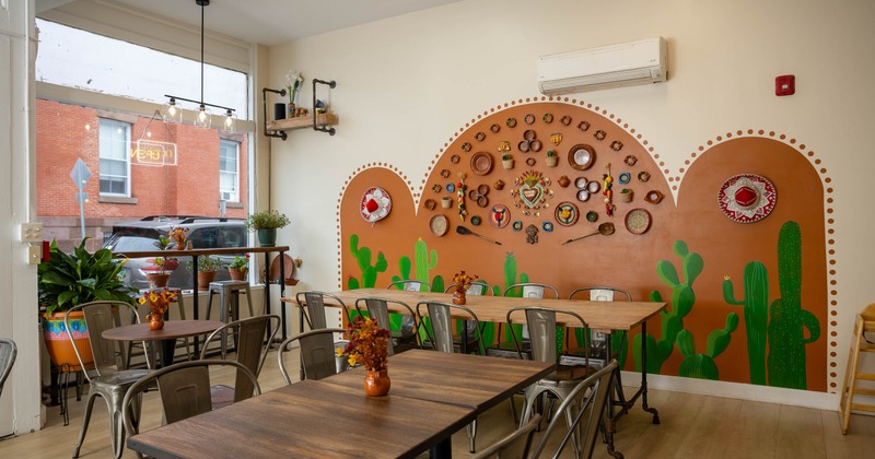 Dining room - wood tables, metal chairs, potted plants, a colorful cactus & folk-art mural