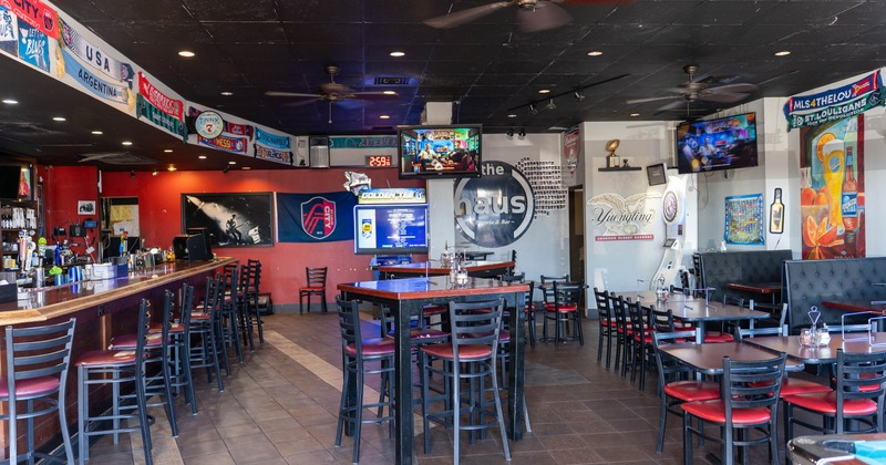 Interior of a sports bar with red accents, TVs, bar stools, and sports memorabilia on the walls