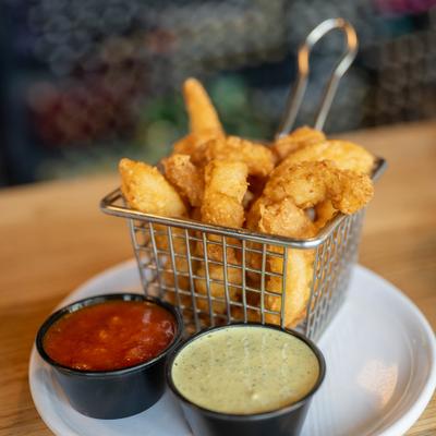 Fried calamari served in a wire basket with dipping sauces on the side.