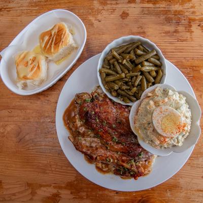 Southern-style meal with baked chicken, potato salad, green beans, and bread rolls.