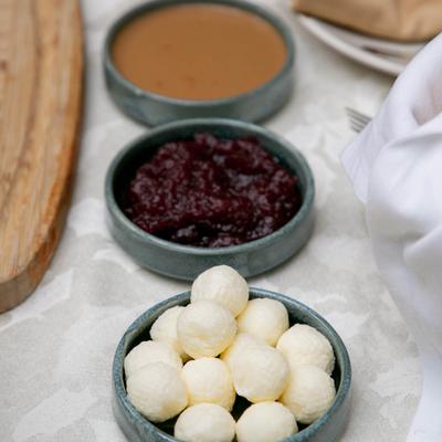 Bowls of butter balls, cranberry relish, and gravy on a table.