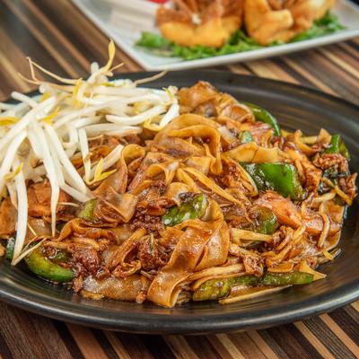 Stir-fried wide noodles with chicken, peppers, and bean sprouts on a black plate.