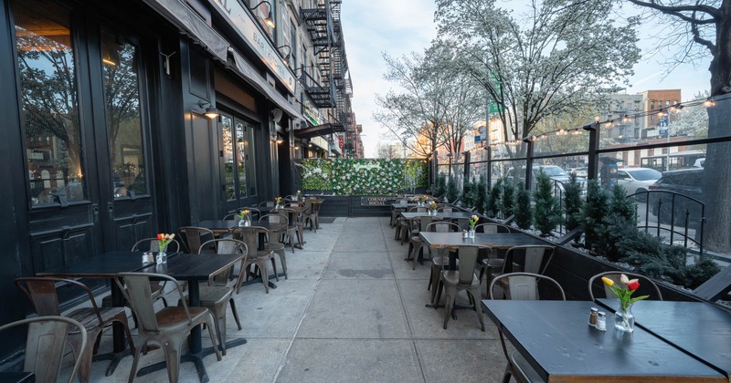 Outdoor dining area with tables and chairs, decorated with flowers and separated by a green wall