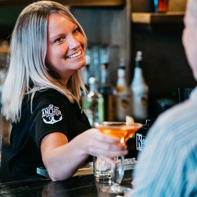 Smiling bartender serves a cocktail to a patron across the bar