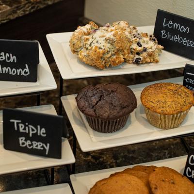 A variety of bakery items, primarily muffins and cookies, on a tiered display stand.