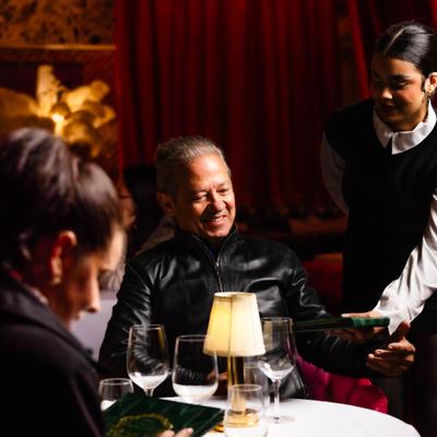 Hostess presenting menus to guests seated at a candlelit dining table.