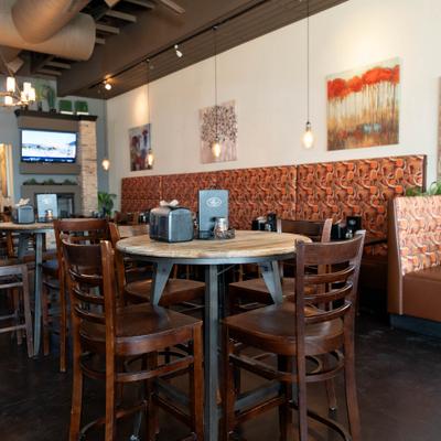 Dining area featuring high-top tables with dark wood stools and a red patterned booths.
