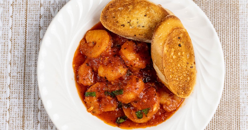 A dish of shrimp in a red sauce served with garlic bread toast