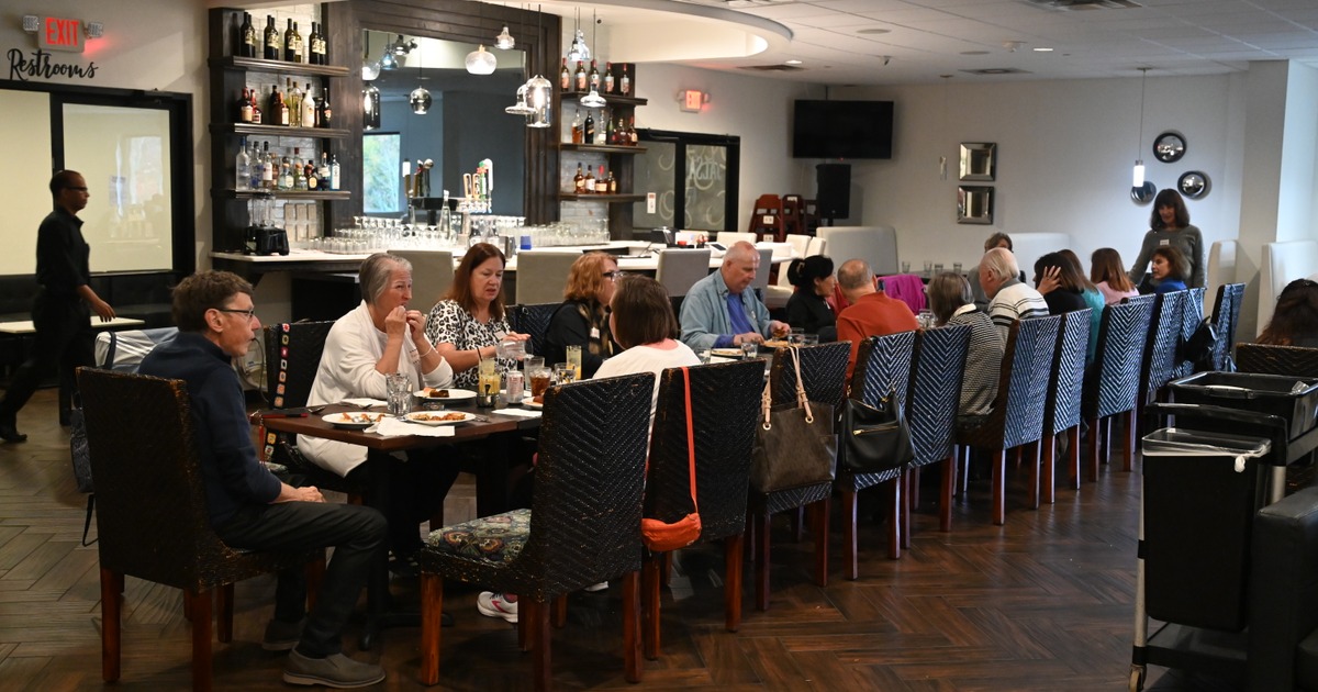 A large group of people is seated at a restaurant table, engaged in conversation and dining