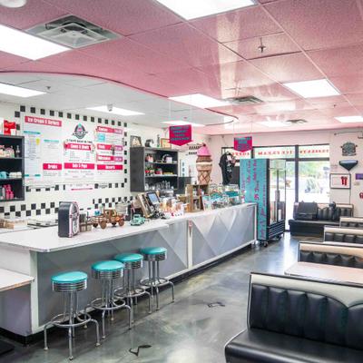 Interior with a teal-cushioned counter, black booths, and a pink ceiling.