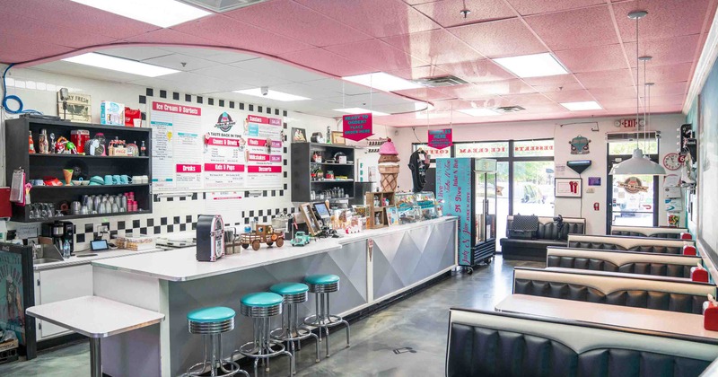 Interior with a teal-cushioned counter, black booths, and a pink ceiling