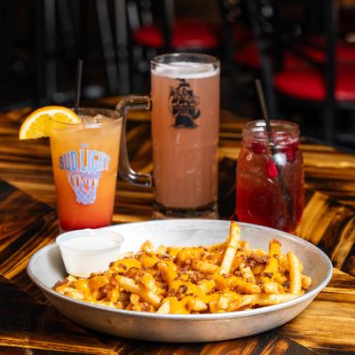 Loaded fries plate accompanied with three colorful drinks in glasses.