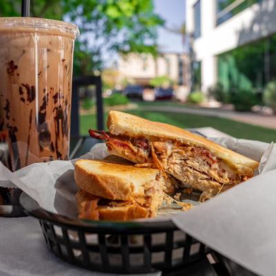 Chicken panini and a cup of iced coffee served on a table outside.