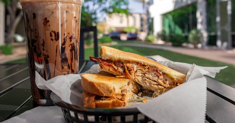 Chicken panini and a cup of iced coffee served on a table outside