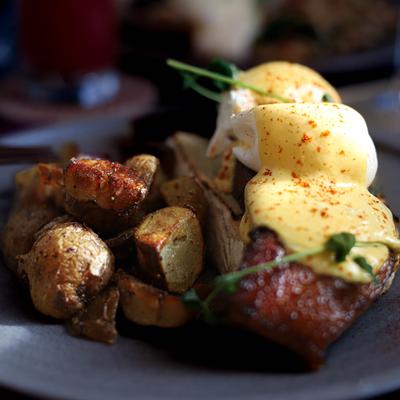 A plate featuring roasted potatoes, bacon, and poached eggs topped with hollandaise and paprika.