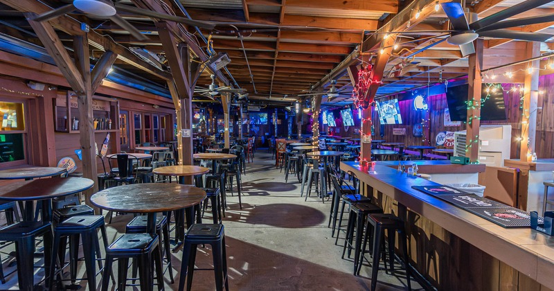 Interior, wooden tables, black stools, colorful string lights, and multiple TV screens