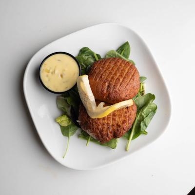 Crab cakes with greens, dipping sauce, and lemon slices.