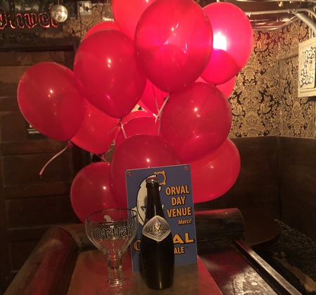 Interior, red party balloons by a table with a bottle of Orval beer