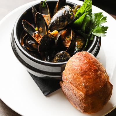 Mussels served in a black pot with bread roll on a plate.