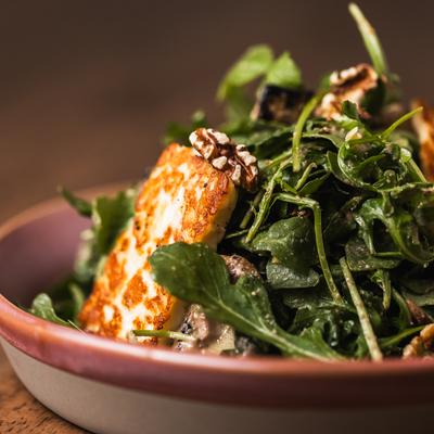 A salad with grilled halloumi cheese and arugula leaves, topped with walnuts.