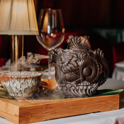 Hand pouring from a dragon teapot into a steaming cup on a tray.