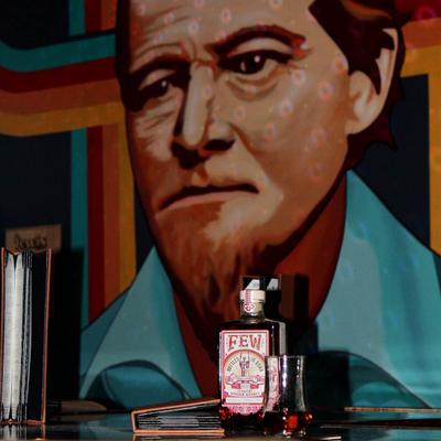 Bottle of bourbon with a glass and pop art mural in the background.
