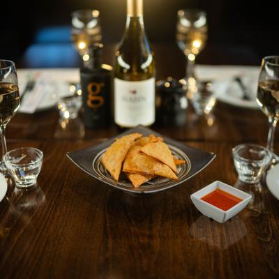 Fried crab rangoon with dipping sauce, served alongside four glasses of wine and a bottle.