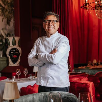 Chef smiling with arms crossed, red curtain and statue behind him.
