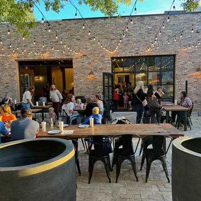 People dining outdoors near brick building with string lights overhead.