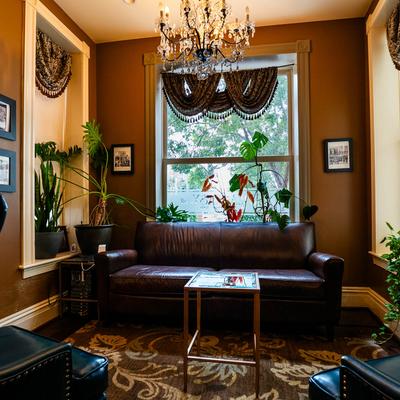 A cozy lounge room featuring a chandelier, a sofa, a chair, decorative plants, and a table.