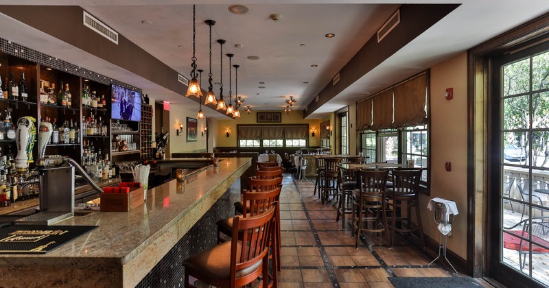 Interior of a modern bar with a granite counter, bar stools, pendant lights and large windows